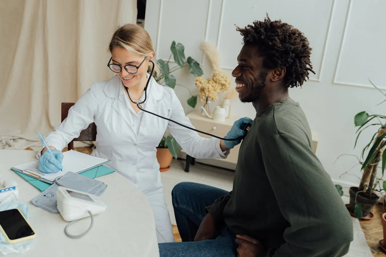 Caucasian female doctor checks black male patients heart rate with stethoscope in a clinic.